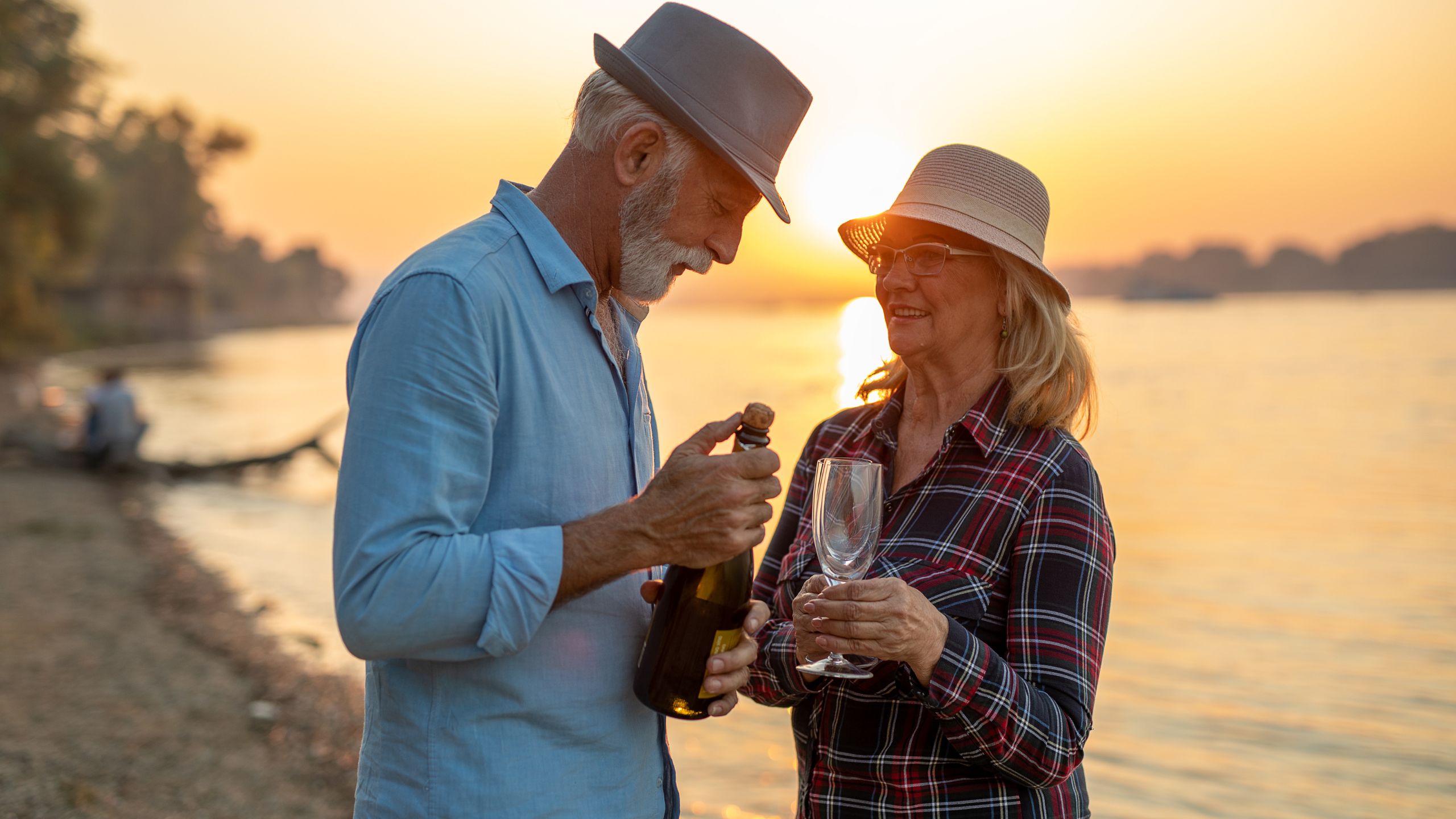 couples celebrate their wedding anniversary holding a glass and a bottle of wine beside a bitch