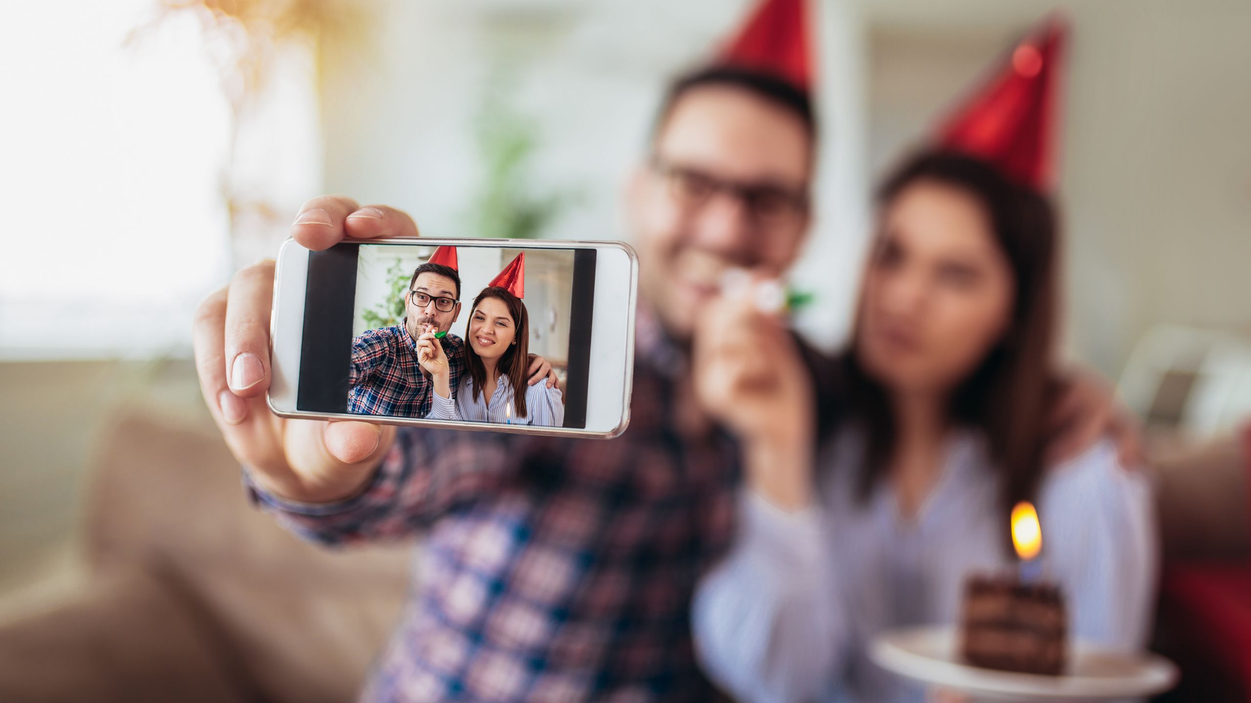 Wife celebrating husbands birthday with both taking a selfie and a cake help by wife with one burning candle