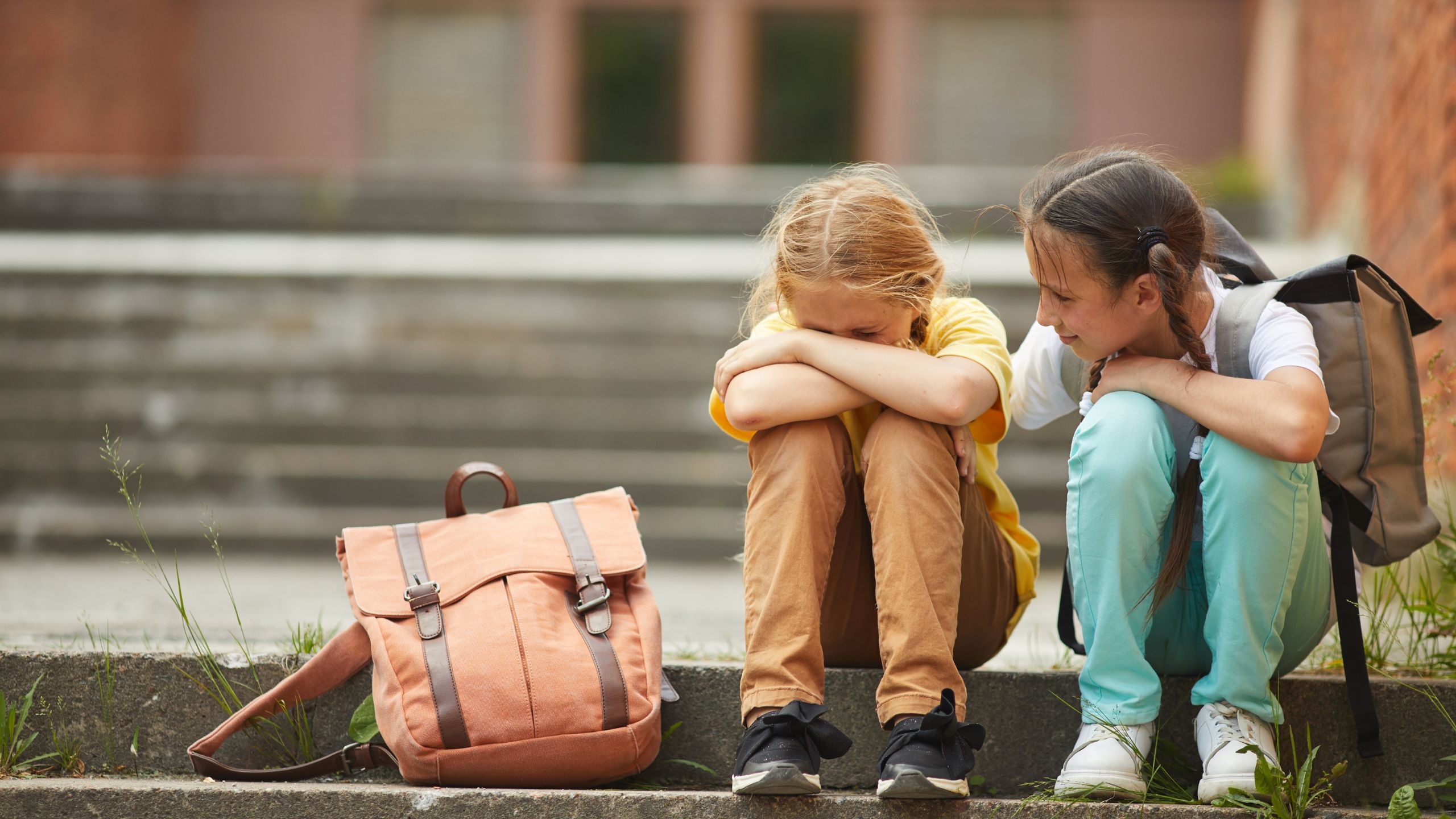 Two friends sitting on out door friends with one comforting her sad friend